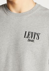 Grå bomullströja med en svart tryckt "LEVI'S"-logotyp och grafik, med rund halsringning och korta ärmar. Slät textur.