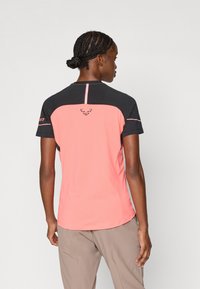 Camisa atlética de mangas curtas em rosa e preto com um logótipo nas costas, gola redonda e detalhes de costura contrastantes.