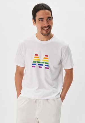 Valge puuvillane t-särk, millel on mitmevärviline triibuline täht "M" punases, oranžis, kollases, rohelises, sinises ja lillakas värvitoonis. Lühikesed varrukad, mugav lõige.