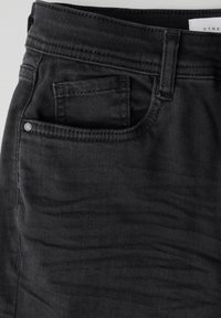 Tessuto denim nero con una consistenza morbida presenta una tasca laterale visibile e dettagli di cucitura sottili. Una borchia metallica abbellisce la tasca.