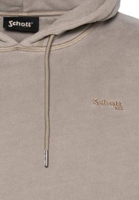Beige Kapuzenpullover mit einer Kordelzugkapuze, subtiler Textur und einem gestickten Logo auf der Brust. Verfügt über eine einzelne metallene Kordelspitze für den Kordelzug.