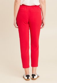 Rode elastische broek met een slim fit, twee achterzakken en een gladde textuur, gecombineerd met witte schoenen met zwarte accenten.