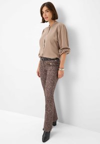 Beige blouse met knopen aan de voorkant en ballonmouwen, gecombineerd met bruine flared broek met luipaardprint, gedragen met zwarte haklaarzen.