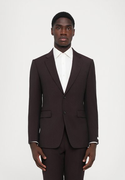 Abito bordeaux scuro con una vestibilità slim, dotato di revers a punta, due bottoni e una camicia bianca sotto. Le maniche accentuate mostrano un bordo bianco.