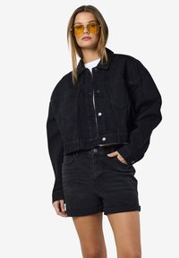 Black denim cropped jacket with button closure and two chest pockets, paired with black denim shorts, ensuring a coordinated monochrome look.