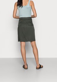 Ljusblå ribbad linne med spetsdetalj, kombinerad med en mörkgrön knälång kjol som har två bakfickor och en rak skärning.