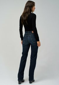 Jeans de mezclilla de color azul oscuro, acampanados y de cintura alta, con bolsillos traseros y detalles de costura sutil, combinados con una blusa negra ajustada de manga larga.