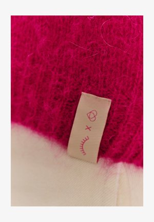 Fuksjowy dzianinowy wełniany materiał o miękkiej fakturze, połączony z kremową bazą tkaniny. Posiada małą beżową metkę z zaokrąglonymi wzorami graficznymi.