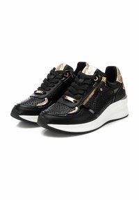 Zapatillas negras con acabado texturizado, que presentan detalles en metal dorado y una cremallera decorativa. Suela de goma blanca con un ligero diseño de cuña.