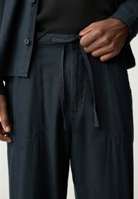 Donkerblauwe broek van zacht materiaal, met een tailleband met trekkoord, zijzakken en subtiele stiksels.