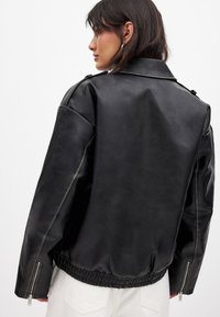 Giubbotto in ecopelle nera con design cropped, caratterizzato da una finitura testurizzata, maniche con cerniera e cintura elastica.