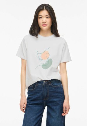 Kvinde iført en hvid t-shirt med minimalistisk abstrakt ansigtslinjekunst i fersken og grøn, kombineret med højtaljede blå jeans.