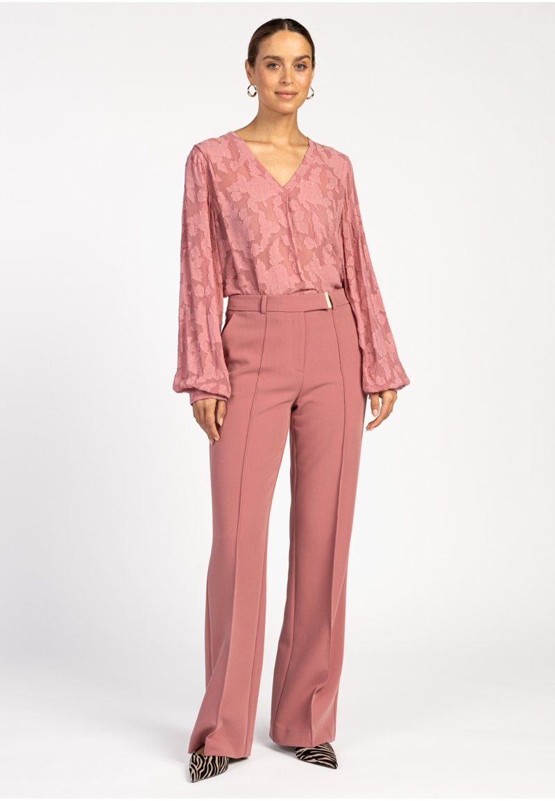 Roze blouse met een patroon, een V-hals en lange mouwen, gecombineerd met hoge taille, ruime broeken in een bijpassende roze tint.