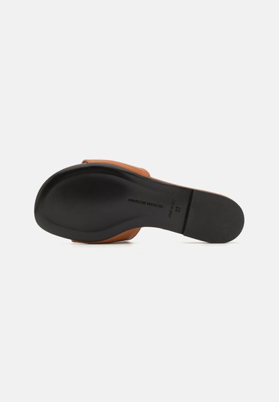 Sandale en cuir marron avec une semelle en caoutchouc noir et lisse. Présente un petit talon et un design minimaliste, soulignant la simplicité et le confort.