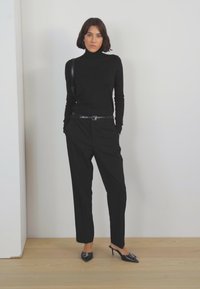 Zwarte coltrui, getailleerde zwarte broek en glanzende zwarte stilettohakken. Eenvoudig ontwerp met een strakke silhouette en subtiele textuur.