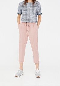 Haut à manches courtes à carreaux bleu et blanc avec un bord à frange, associé à un pantalon rose ajusté avec un lien à l'avant et des ourlets retroussés. Baskets grises.