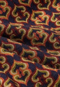 Mönstrad tyg med sammanflätade kurvor i röd, orange, gul och mörkblå. Den texturerade väven skapar djup och visuell intresse.