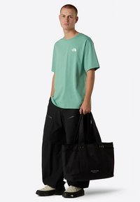 Mintgrøn kortærmet t-shirt med hvidt logo, sorte løstsiddende bukser og en sort stofnettaske med metaldetaljer og logodetalje.