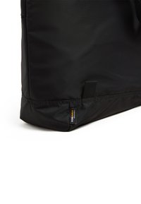 Sac fourre-tout en tissu noir avec une texture lisse, arborant une étiquette Cordura sur le côté et une couture en bas. Le design est simple et pratique.