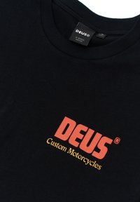 Black cotton t-shirt featuring a prominent red "DEUS" logo and yellow "Custom Motorcycles" text, crew neck design. Smooth texture.