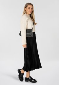 Maglione crema, gonna midi plissettata nera, scarpe lucide nere con suola spessa e una borsa intrecciata bianca e nera con tracolla.