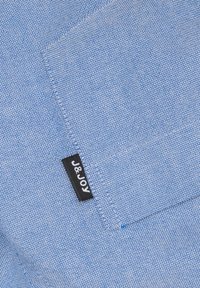 Close-up van een blauw gemerkt stof met een gestikte zak en een klein zwart label met de tekst "J&Joy" dat aan de rand van de zak is genaaid.