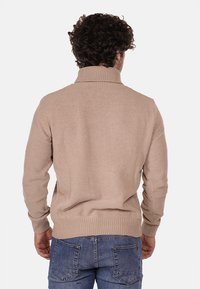 Maglione beige a maglia con colletto alto e polsini a costine, caratterizzato da un motivo testurizzato. Indossato con jeans in denim blu.