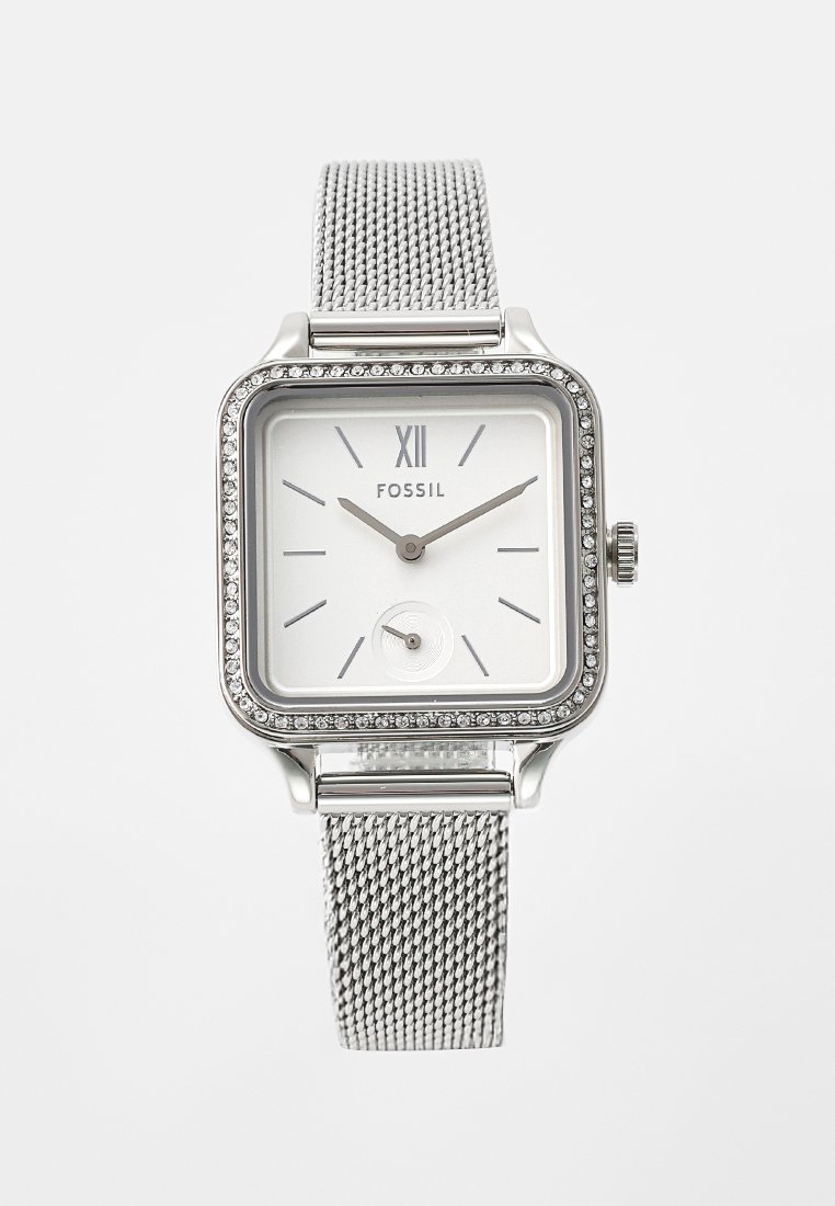 Srebrny kwadratowy zegarek z siatkowym paskiem, białą tarczą, rzymską cyfrą XII, minimalistycznymi wskazówkami i bezelą zdobioną kryształkami. Marka: Fossil.