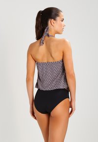 Schwarze Badeshort kombiniert mit einem gemusterten Neckholder-Oberteil, das geometrische Formen in Marineblau, Pink und Creme zeigt, mit einer gebundenen Schleife am Hals.
