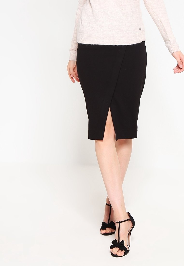 Svart pennkjol med sidofåra. Tyget är slätt med en tätsittande design. Bärs med högklackade skor med ankelrem och rosett.