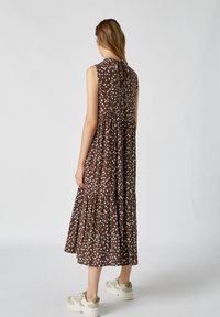 Brun, ärmlös klänning med vita prickar, lagrad design och en nyckelhålsöppning bak. Buren med ljusa sneakers.