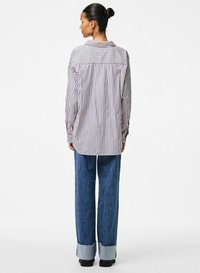 Camicia a righe bianca e blu navy, con maniche lunghe, colletto classico e vestibilità comoda. Abbinata a jeans blu a gamba larga con orli risvoltati.