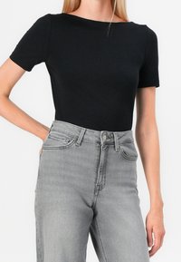 Top nero a maniche corte con scollo ampio abbinato a jeans grigi a vita alta. Materiale in cotone con una texture morbida e vestibilità classica.