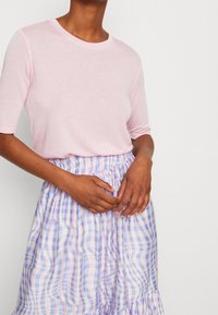 Top rosa chiaro a maniche corte abbinato a una gonna a quadri dai colori vivaci con motivo ondulato, caratterizzata da una fascia elastica aderente in vita e un orlo arricciato.