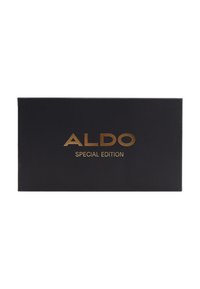 Boîte noire à finition mate, avec un texte doré en relief au centre indiquant "ÉDITION SPÉCIALE ALDO".