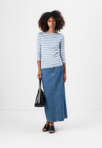 Stripet langermet skjorte i lys blå og hvit, kombinert med et langt denims skjørt, svart tote veske og svarte sandaler.