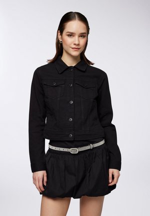 Giubbotto in denim nero con colletto, chiusura frontale con bottoni, due tasche sul petto e maniche lunghe, indossato sopra una gonna nera e una cintura.