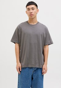 Graues Baumwoll-T-Shirt mit rundem Ausschnitt und kurzen Ärmeln, das eine lockere Passform und minimale Nähdetails aufweist. Getragen mit blauen Jeans.