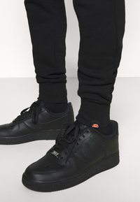 Svarta lädersneakers med rund tå och platt sula, med svarta snören och varumärkesdetaljer. Svarta joggers med ribbade muddar.