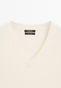 V-Ausschnitt-Pullover aus 100% Kaschmir; weicher, leichter Stoff in Off-White mit geripptem Kragen und Etikettendetails auf der Innenseite.