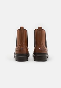 Stivaletti in pelle marrone con pannelli laterali elasticizzati, suole in gomma e dettagli con marchio sul tallone. Superficie liscia con design elegante.