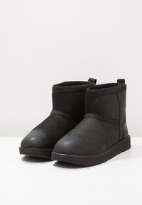 Czarne botki na kostkę wykonane z gładkiego zamszu, z zaokrąglonym noskiem, płaską podeszwą oraz prostym designem z krótkim, podwiniętym wykończeniem.