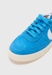 Baskets en suede bleu avec logo blanc, tige texturée et lacets assortis. Dotées d'une semelle en caoutchouc crème texturée. Vue en gros plan.