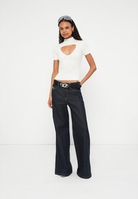 Λευκό ριμπ κορμάκι με σκίσιμο, σε συνδυασμό με σκούρα μπλε τζιν παντελόνι με φαρδιά μπάτσα. Μαύρη ζώνη με εμφανή αγκράφα. Διαυγή γυαλιά ηλίου ολοκληρώνουν το σύνολο.