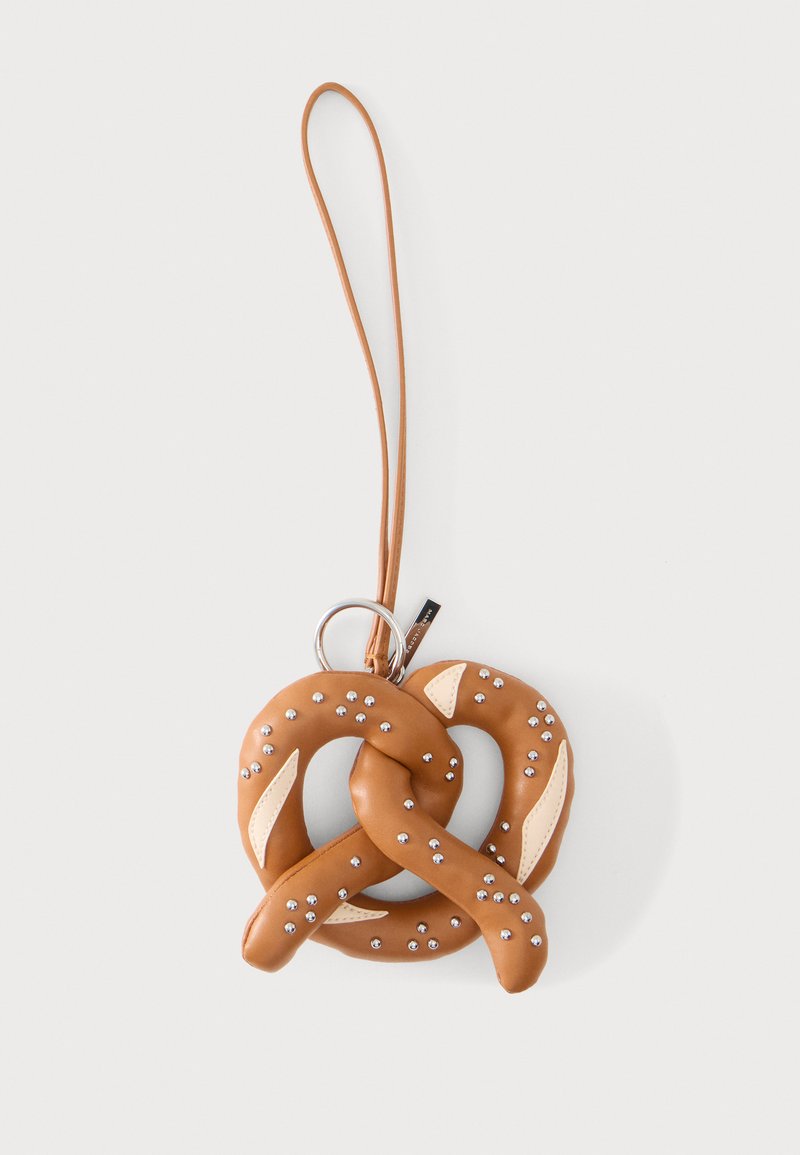 Porte-clés en cuir marron en forme de bretzel avec des clous argentés et une lanière en cuir passée dans un anneau métallique sur fond blanc.
