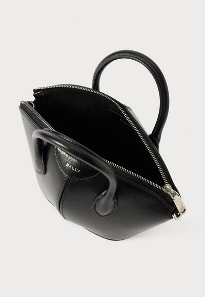 Sac à main en cuir noir avec une forme arrondie, des poignées doubles et une fermeture éclair. La doublure intérieure est en suède noir. Détails en matériel argenté.