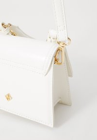 Sac à main en cuir blanc au design structuré, avec une fermeture rabat et des accents dorés, y compris la quincaillerie et les coutures.