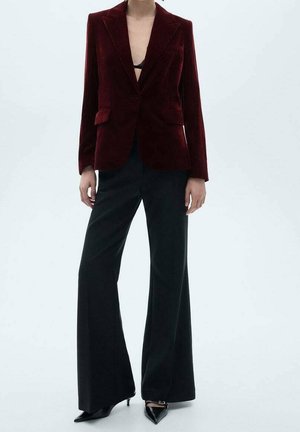 Person wearing a burgundy velvet blazer, black wide-leg trousers, and black pointed heels, standing against a plain light background.