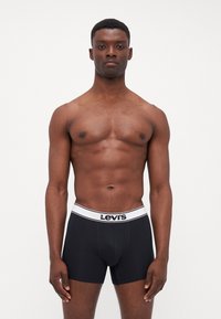 Črne bombažne bokserice z belim elastičnim pasom, na katerem je napis "Levi's". Gladka tekstura, prilegajoča zasnova in dolžina do sredine stegen.