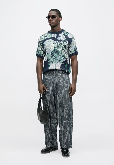 Μπλε σκούρο πλεκτό μπλουζάκι με λουλουδάτο σχέδιο και κοντά μανίκια, σε συνδυασμό με γκρι φαρδιά παντελόνια με υφή σχεδίου. Μαύρη τσάντα και παπούτσια ολοκληρώνουν το σύνολο.